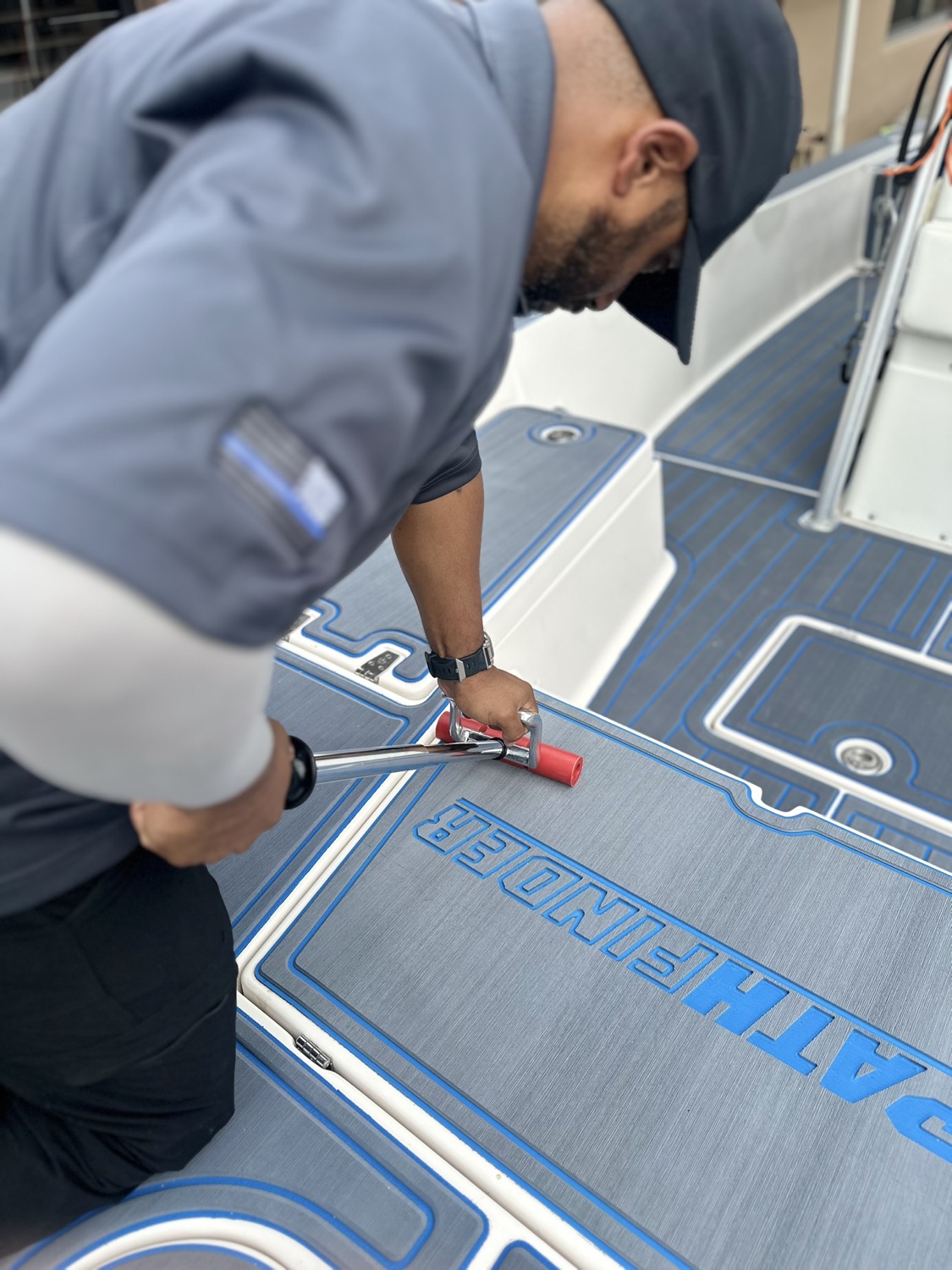 A Treadic installer rolling down a custom gray and blue EVA foam deck panel with a routed boat name
